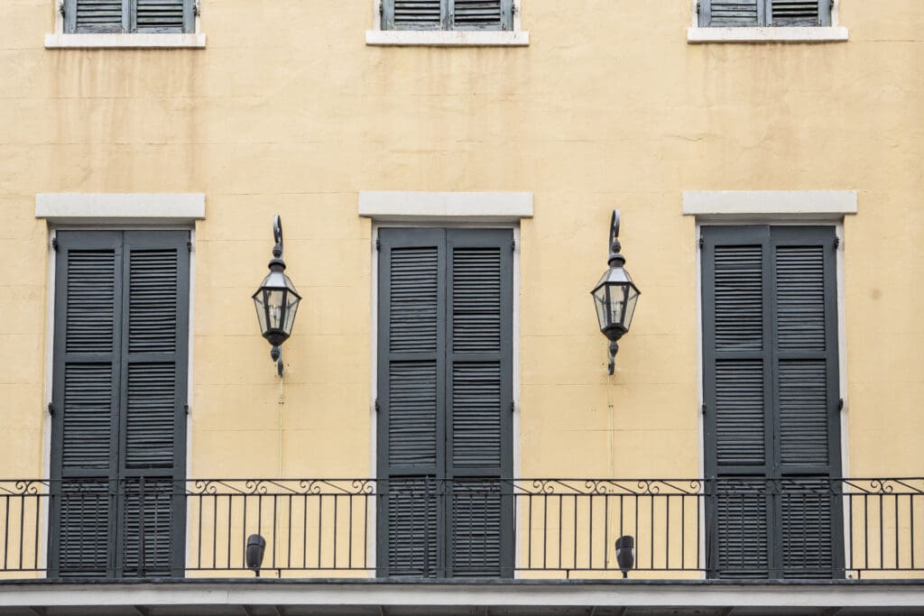 Yellow French Quarter house balcony with closed gray shutters and hanging lights