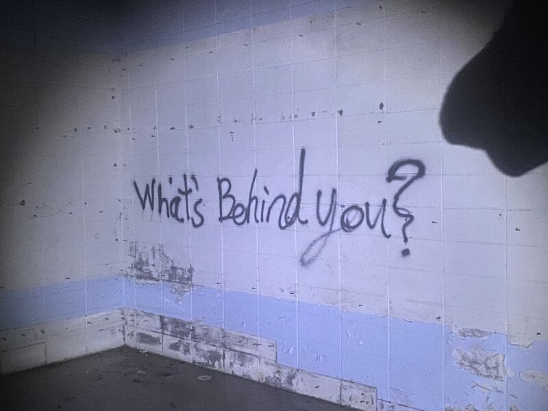 Tile wall with "What's Behind you?" spray painted in black