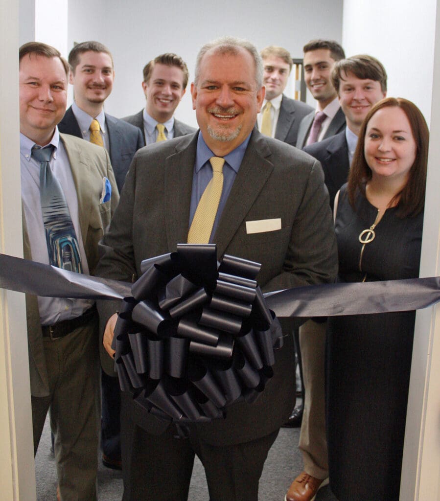 Mosaic Property Valuations team stands in a group behind a large black ribbon across the doorway at their new office ribbon cutting